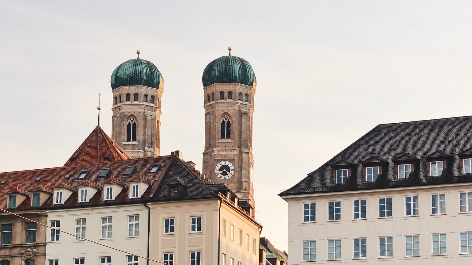 Die Türme der Frauenkirche mit ihren grünen Hauben über den Dächern der Münchner Altstadt. Mit KI erstellte Darstellung.